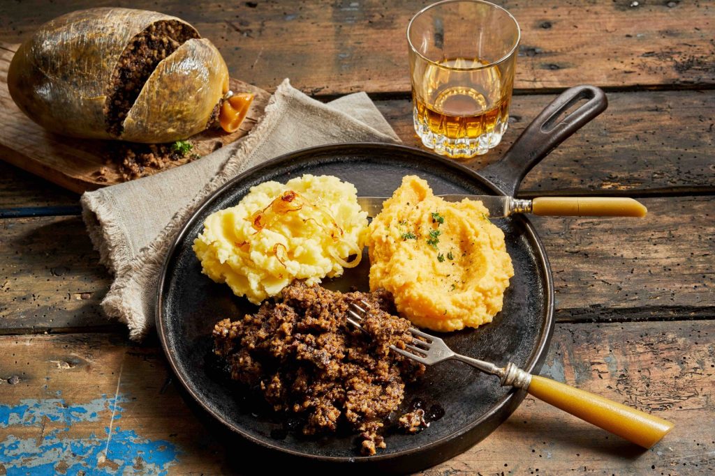 Rustic meal of haggis, neeps and tatties served with a tumbler of whisky to celebrate Robert Burns Supper in a high angle view