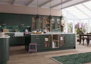 The Georgina shaker kitchen door in Deep Forest Green is showcased in this kitchen design. A striking green kitchen with an island, pendulum gold lighting and gold handles. A pink stool is showcased alongside the green kitchen in this kitchen design created by The Kitchen Depot