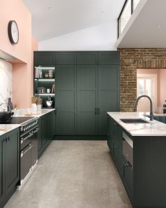 Alana Heritage Green shaker kitchen by The Kitchen Depot with white worktops above oven and pink walls.