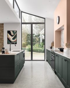 Alana Heritage Green shaker kitchen by The Kitchen Depot in room with pink painted walls and large open window doors.