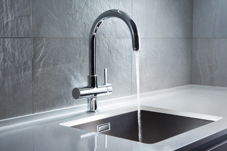 Stainless steel sink and tap with running water and white worktops