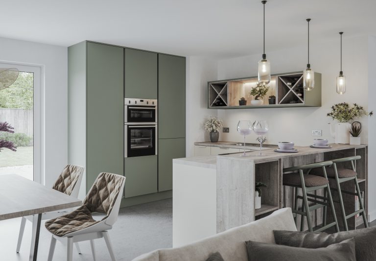 A discovery kitchen range is shown with Reed Green and Taupe units, wooden kitchen island and with shelving either side containing potted plants, cook books and lavender blankets. The seating area of the island has 2 reed green bar stools. Above the kitchen island are 3 lantern lights. The back units are reed green and true handleless tall units with a stainless steel double oven placed in the middle of the units.